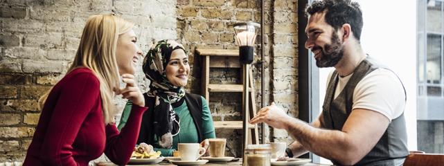 Three people sitting at a table talking and drinking coffee.